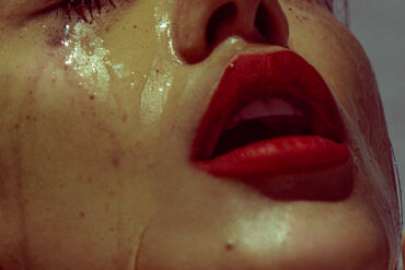 Model with red lipstick and water running down her face, almost looking like tears