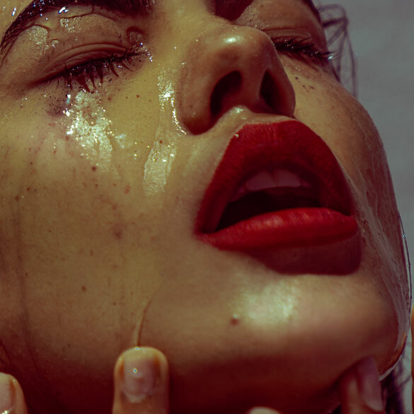 Model with red lipstick and water running down her face, almost looking like tears