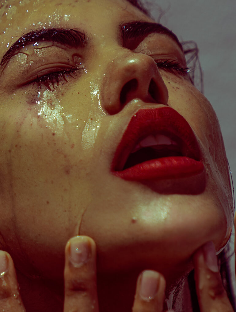 Model with red lipstick and water running down her face, almost looking like tears